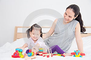 Little girl playing toys with her mother on bed at home