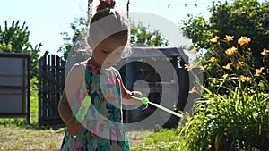 Little girl playing in the village in summer day with soap bubbles.