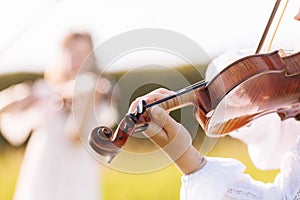 little girl is playing violin outdoor with garden in the background on sunny summer day. Image with selective focus and