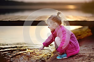 Little girl playing with water and stick during walk by the lake