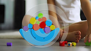 Little girl playing with wooden balancing toy on the floor in home living room. Focus on balancer