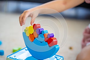 Little girl playing with wooden balancing toy on the floor in home living room. Focus on balancer