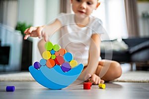 Little girl playing with wooden balancing toy on the floor in home living room. Focus on balancer