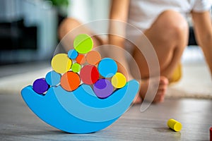 Little girl playing with wooden balancing toy on the floor in home living room. Focus on balancer