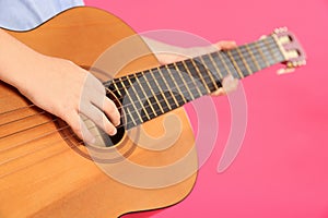Little girl playing wooden guitar on color background