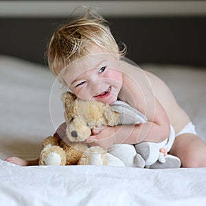 Little girl plays in bed with teddy bear