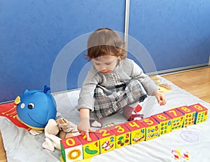 The little girl plays with cubes, sitting on a floor