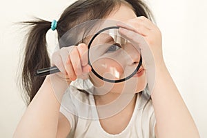 Little girl plays a detective. A child examines something through a magnifying glass. A girl with two ponytails plays