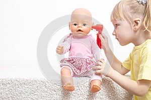 A little girl plays with a doll examines her ears. The concept of pediatric otolaryngology in medicine, treatment of otitis media