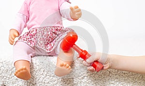 A little girl plays with a doll, and with a small neurological hammer, hits the knee of the doll. Child neurology