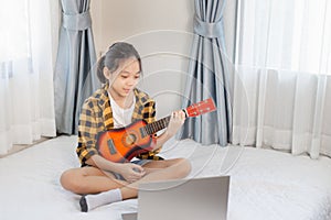 Little girl plays the guitar, child girl learning to play the guitar in the bedroom, Hobby for children