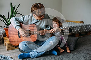 Little girl plays the guitar with her mother on the floor at home