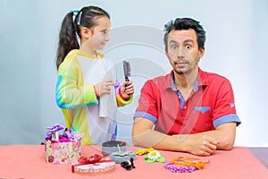 Little girl plays with her father at home in a beauty salon, combing her hair