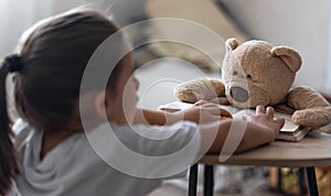 A little girl plays with her teddy bear, teaches him to read