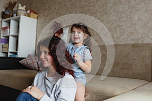 a little girl plays at home with her mother doing her hair while combing her mother s long hair