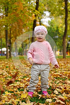 Little girl plays with maple leaves in autumn