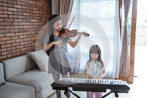 Little girl plays a musical instrument piano with her sister playing the violin together