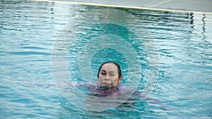 Little girl plays in the outdoor swimming pool of tropical resort during family summer vacation.