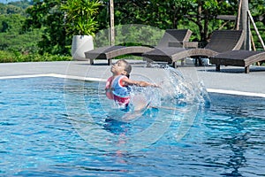 Little girl plays in the outdoor swimming pool of tropical resort during family summer vacation. Kids learning to swim. Healthy