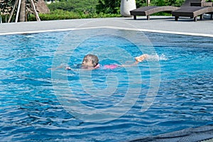 Little girl plays in the outdoor swimming pool of tropical resort during family summer vacation. Kids learning to swim. Healthy