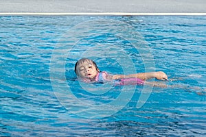 Little girl plays in the outdoor swimming pool of tropical resort during family summer vacation. Kids learning to swim. Healthy