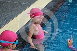 Little girl plays in the outdoor swimming pool of tropical resort during family summer vacation. Kids learning to swim. Healthy