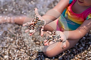 A little girl plays on a pebble beach. The development of fine motor skills. Large grains of sand on the beach