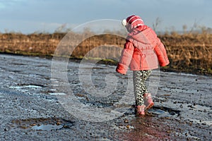 Little girl plays in puddle, children, fun, unforgettable moments, dirty and wet shoes, fun with father, life in village, sunlig