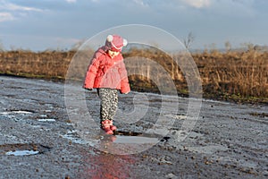 Little girl plays in puddle, children`s fun, unforgettable moments, dirty and wet shoes, fun with father, life in village, sunlig