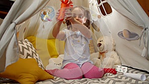 Little girl plays space aliens at home sitting in a tent.