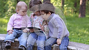 Little girl plays with tablet PC, boy and little girl look at it
