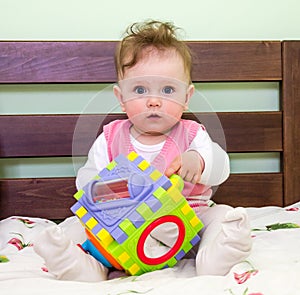 Little girl plays a toy baby on the bed