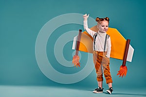 Little girl plays with toy wings on a blue background. A happy child in an astronaut costume plays and dreams of becoming an