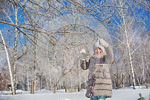 Little girl plays with tree in winter park in sunny day