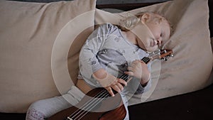 Little girl plays the ukulele and goes to sleep look at the camera