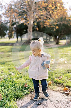 Little girl with a plush cat in her hand walks through the autumn park looking at the fallen leaves
