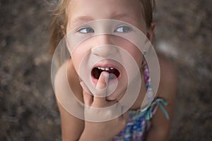 Little girl points the finger at a wobbly baby tooth photo