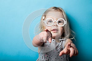A little girl points with fingers and hands. Toy fashion glasses