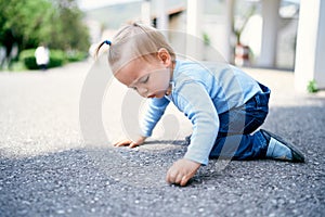 Little girl with a ponytail sits on her knees on the road in the park