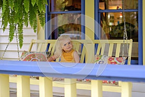 Little girl on a porch swing on a summer day