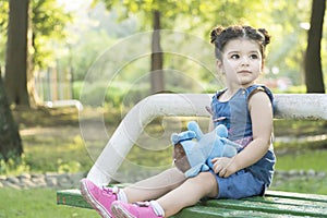 Little girl portrait seated on park bench and  holding a blue elephant doll at hand