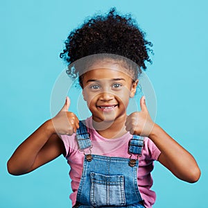 Little girl, portrait smile and thumbs up for winning, good job or success against a blue studio background. Happy child