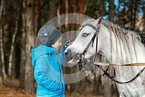 Little girl portrait, stands next to a white pony close-up on the background of nature. Jockey, epodrome, horseback riding