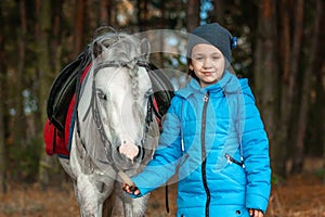 Little girl portrait, stands next to a white pony close-up on the background of nature. Jockey, epodrome, horseback riding