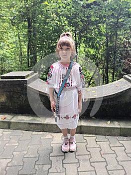 The little girl posing dressed in a traditional white Romanian costume with red flowers, matched with a traditional bag