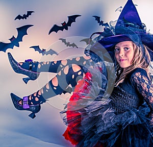 Little girl posing in Halloween witch costume with witch hat and witch shoes
