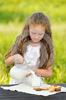 Little girl pouring milk in glass outdoor summer