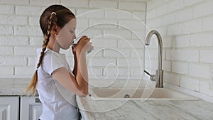 Little girl pouring water from a tap into a glass and drinking. tasteless bad water