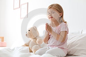 Little girl praying in bed at home. Space