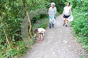 Little girl, pregnant mother and grandmother cleaning the forest of plastics